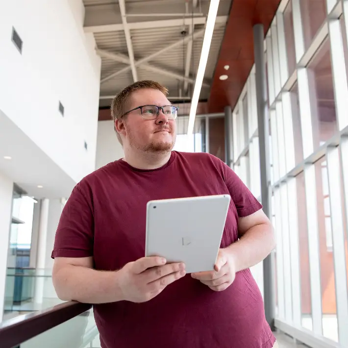 Sean Clarke holding an iPad in the hallway of the College