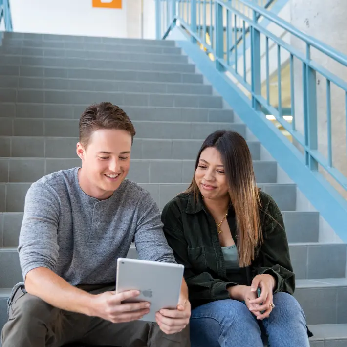Two students sitting on staircase looking at an ipad