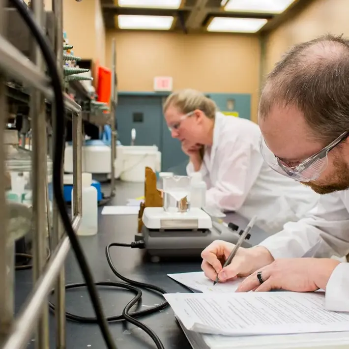 Student in lab coat taking notes at a lab desk