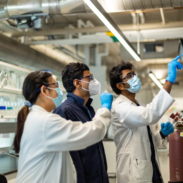 Three people in lab coats in a lab working on a computer