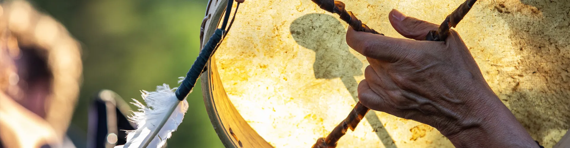 indigenous-ceremonial-drums A close-up photo of a hand using a ceremonial drum with feathers on it.