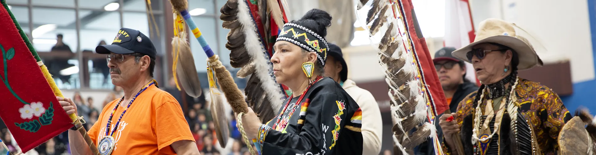 indigenous-PowWow A group of indigenous peoples in a pow wow ceremony holding poles.